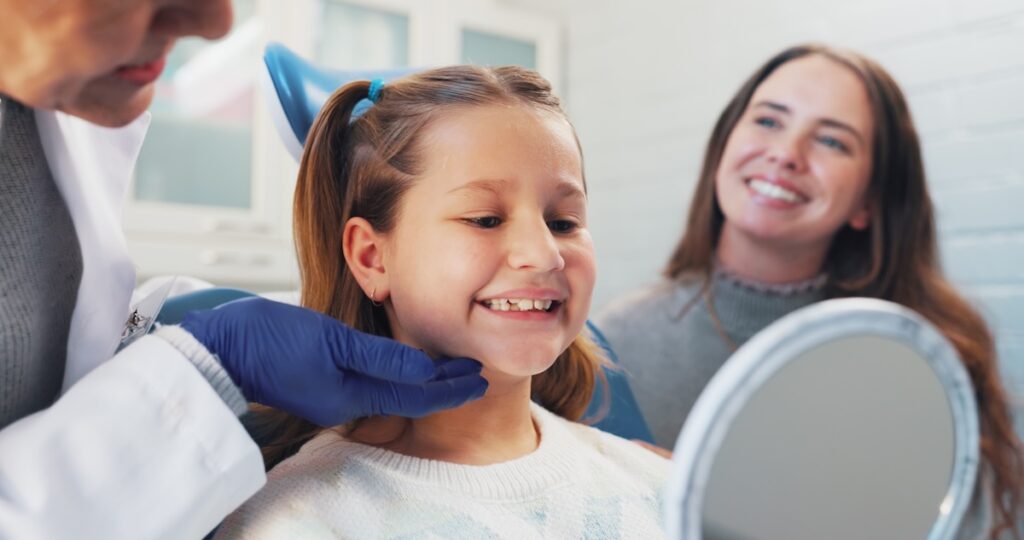 Happy child, dentist and mirror for oral hygiene or teeth health with advice from orthodontist. Girl, family or woman in clinic for dental care, wellness and results or education on cleaning